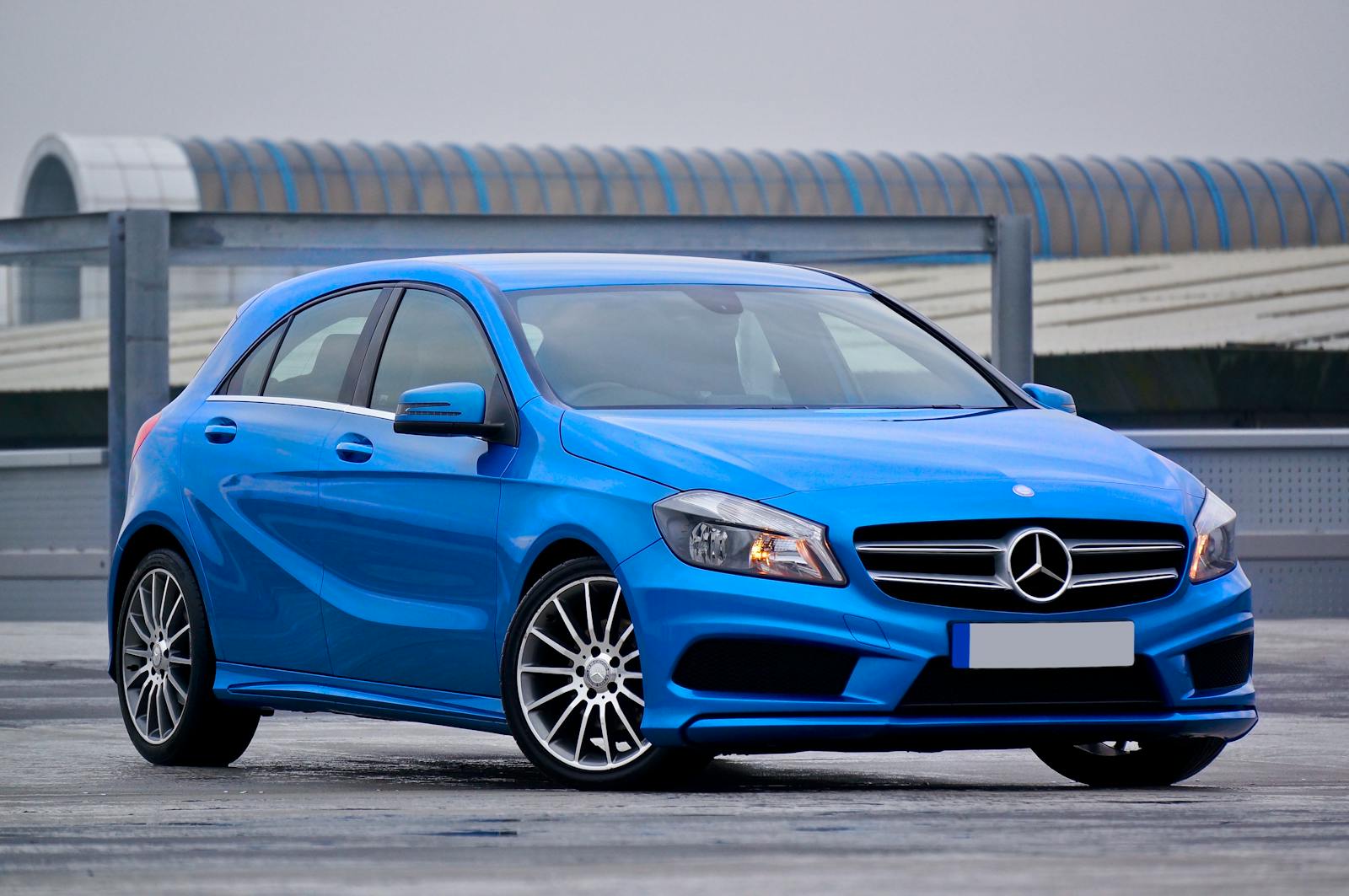 Auto Insurance, Elegant blue Mercedes-Benz hatchback parked outdoors with a modern architectural backdrop.